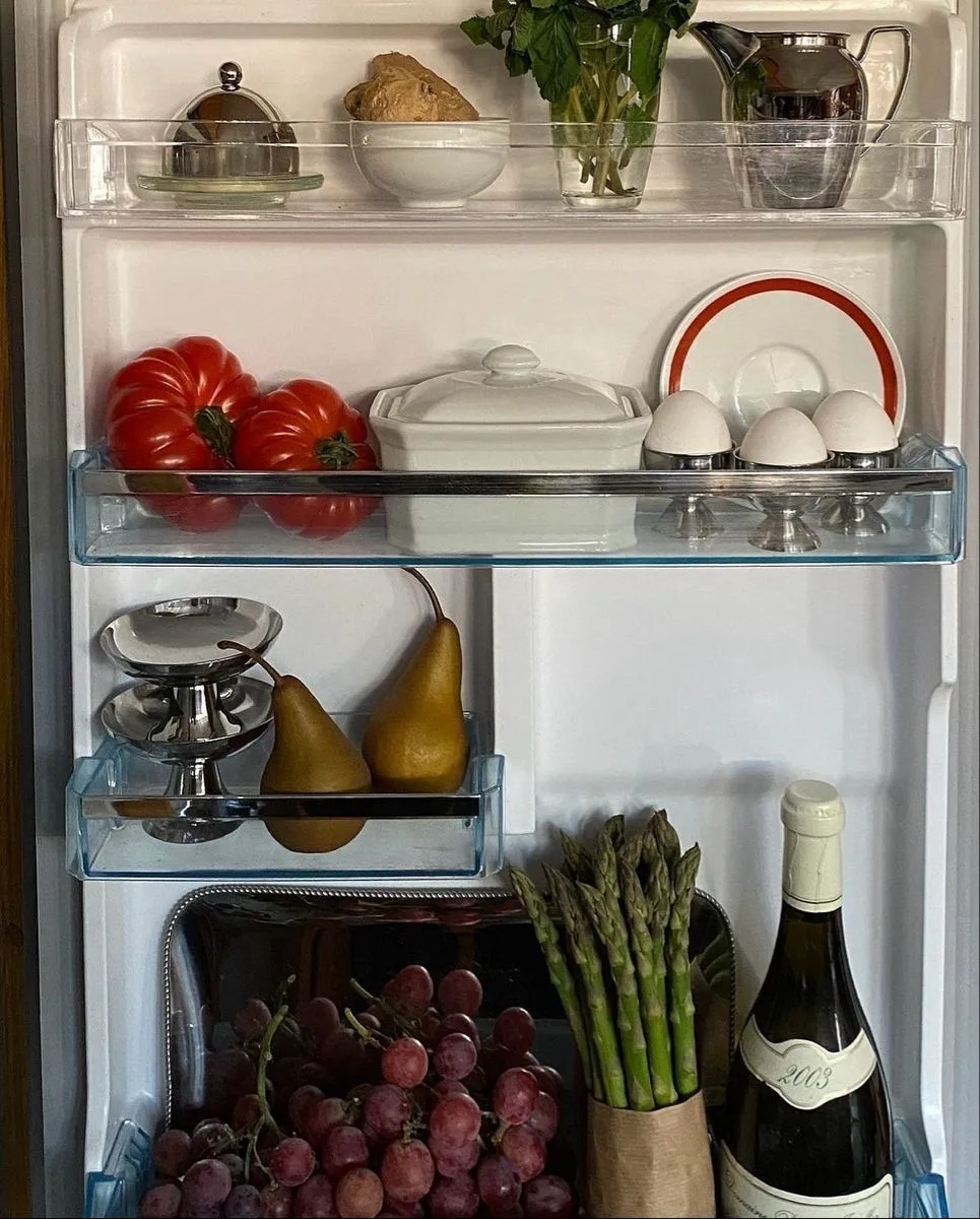 An open refrigerator neatly stocked with fresh produce, eggs, tomatoes, pears and asparagus